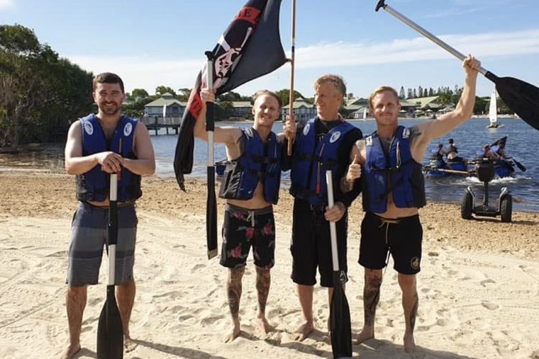 A group with paddles on the beach after a raft build